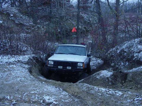 1992 Ford Bronco - A white Jeep Cherokee tackles a challenging off-road trail during winter conditions.