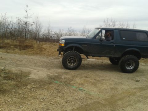 1995 Ford Bronco - A lifted Ford Bronco navigates a dirt path under an overcast sky.