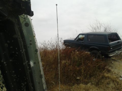1995 Ford Bronco - A dark blue SUV navigates a grassy hill under an overcast sky.