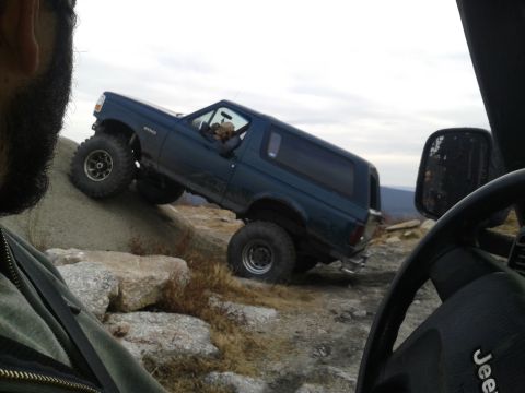 1995 Ford Bronco - A dark blue Ford Bronco is angled precariously on a rocky incline, with its front tires gripping the slope. The image is taken from the per…