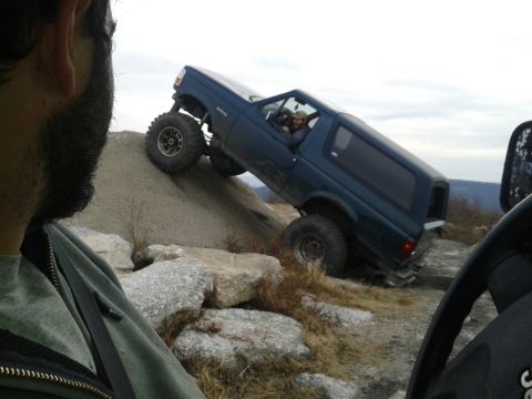 1995 Ford Bronco - A dark blue Ford Bronco is angled precariously on a steep, rocky incline, with its front wheels on a gravel pile and its rear wheels on roc…