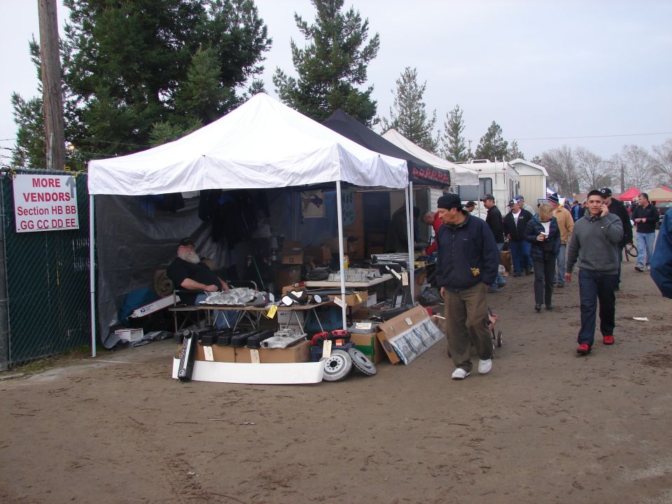 Outdoor swap meet scene with tents and people browsing parts