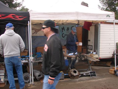 1973 Ford Ranchero - A scene at an outdoor market displays various auto parts for sale under tents, with people browsing.