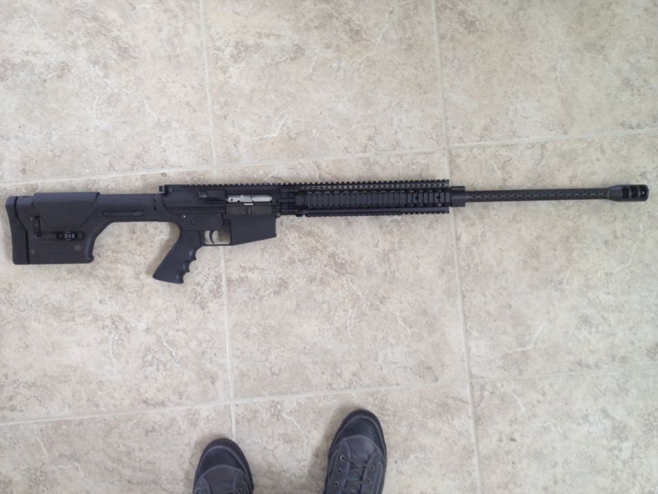 Black rifle with adjustable stock and long barrel, lying on tiled floor