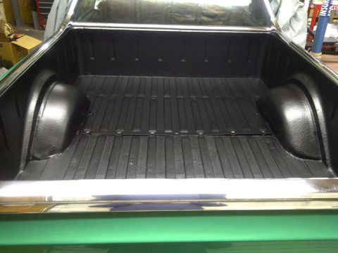 1971 Ford Ranchero - The black-lined truck bed of a green 1971 Ford Ranchero shows its chrome rails and wheel wells.