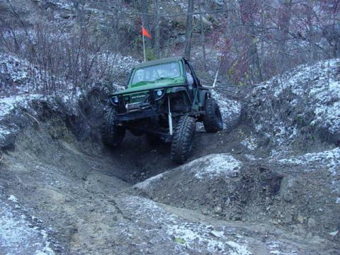 1992 Ford Bronco - A green off-road vehicle tackles a challenging muddy and snowy incline during an off-road excursion.