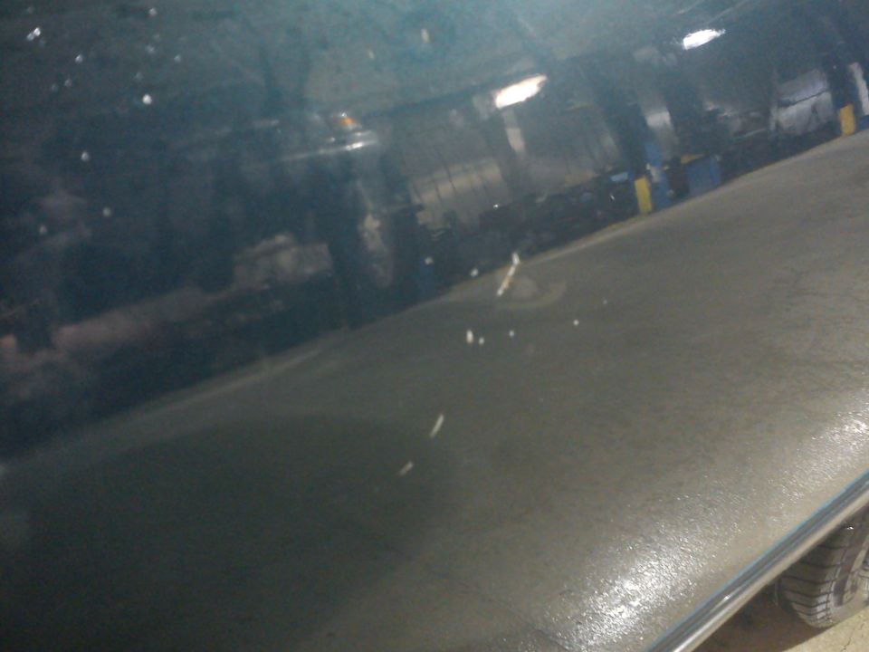 Blurry close-up of a dark car body panel reflecting a garage interior, tire visible at bottom right