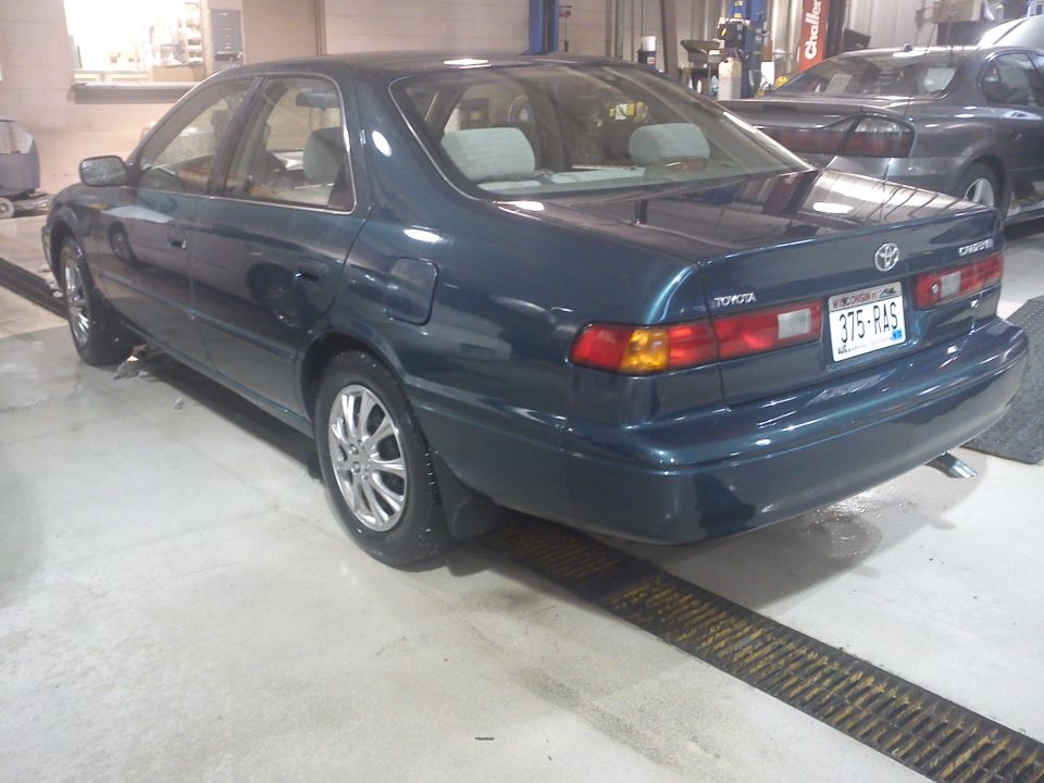 Dark teal 1998 Toyota Camry sedan, rear 3/4 view, parked indoors on a lift