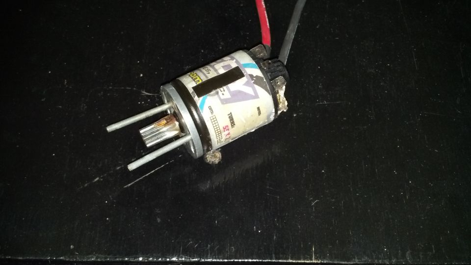 Electric motor with two metal prongs and wires attached, sitting on a dark surface