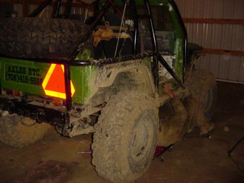 1992 Ford Bronco - A person works on the undercarriage of a heavily modified green off-road vehicle with a roll cage and large tires.