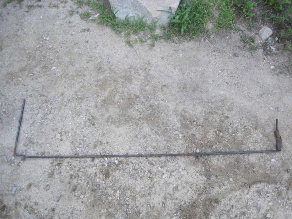 metal rod with two 90-degree bends and a small attachment on one end, lying on dirt ground