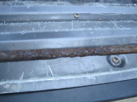 1993 Ford Bronco - Close-up of a rusty metal strip attached to a vehicle's body panel, showing wear and tear.