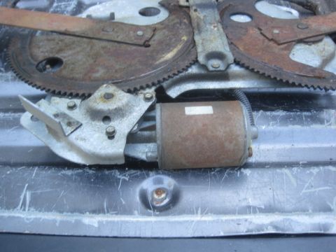 1993 Ford Bronco - A close-up view of a rusty window regulator motor and associated gears.