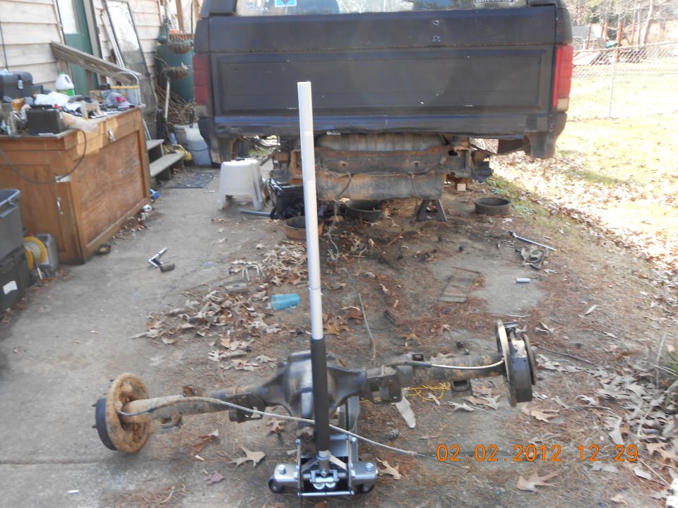 Truck frame with rear axle assembly removed and on a jack. Tools and debris are scattered around