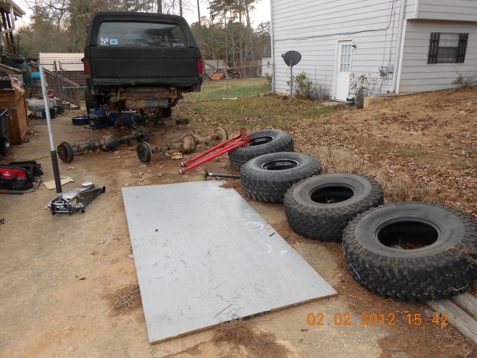 Black SUV with rear axle removed, jack, and tires on the ground