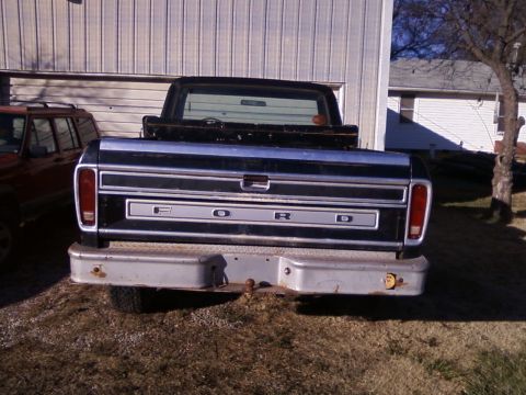 1977 Ford F-150 - The rear of a black Ford F-150 pickup truck is shown parked in front of a building, with another vehicle to its left.