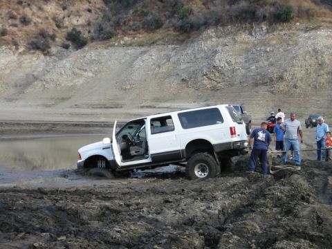 1985 Ford Bronco - A group of people attempt to pull a white SUV out of a muddy, watery area.