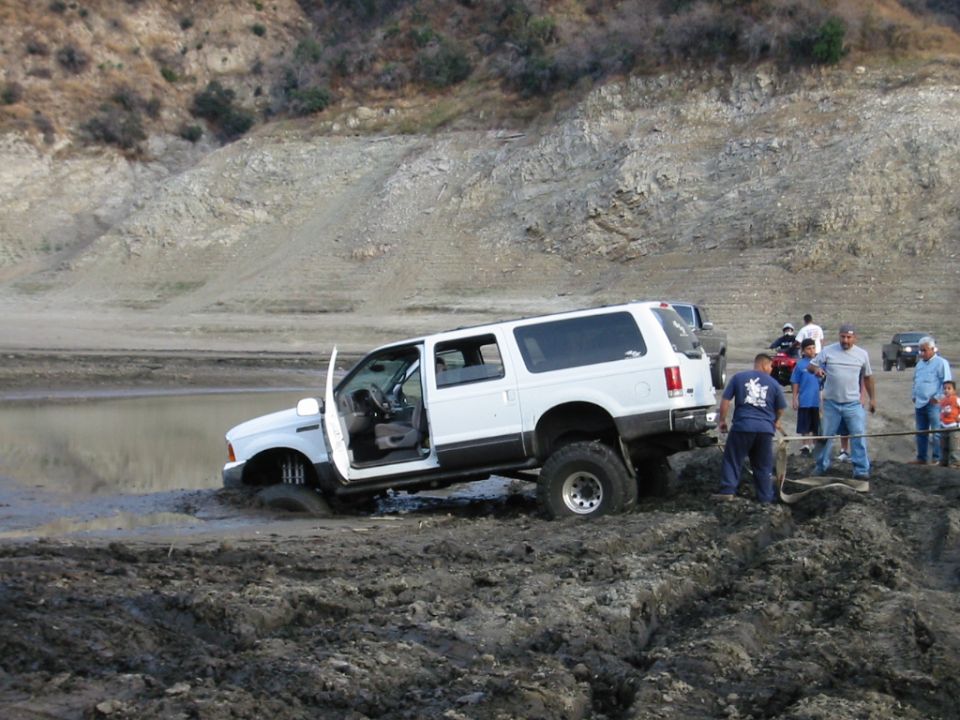 White SUV stuck in deep mud with people gathered to help free it