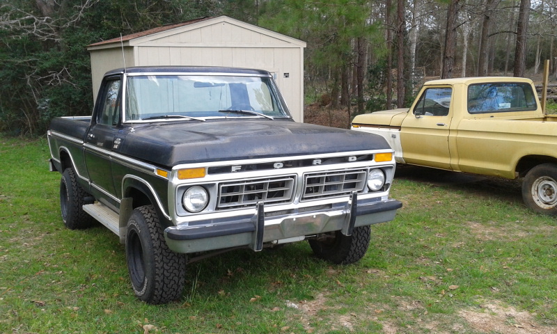 Black 1977 Ford F-150 truck, front quarter view, parked on grass next to a yellow truck