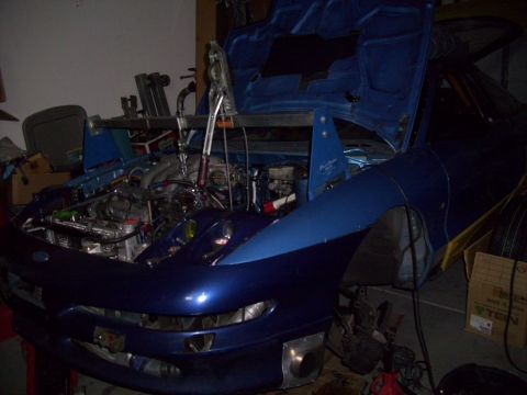 1995 Ford Probe - A blue 1995 Ford Probe is undergoing repairs in a garage, with its hood and engine visible.