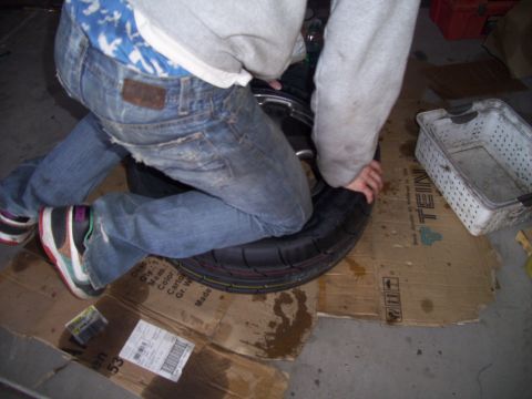 1995 Ford Probe - A person is working on a motorcycle wheel, surrounded by cardboard and a white basket.