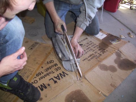 1995 Ford Probe - Two individuals are seen cutting a car part on the floor, which is covered with cardboard and oil stains.