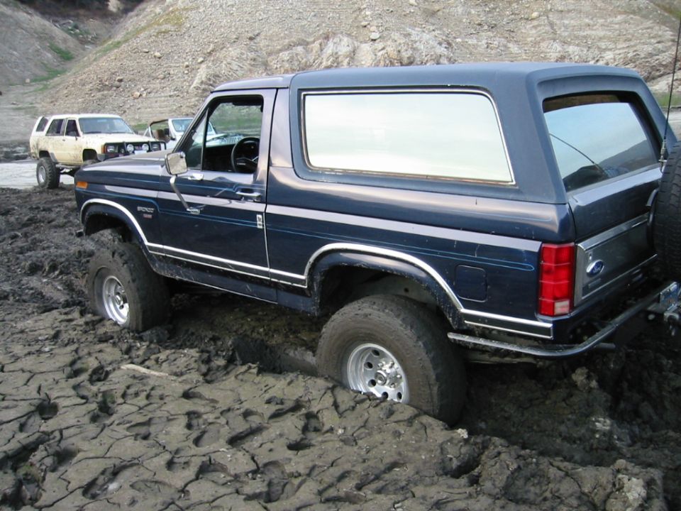 Dark blue Ford Bronco SUV stuck in deep mud, rear 3/4 view
