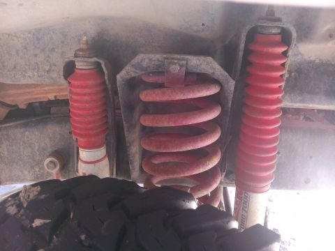 1979 Ford Bronco - Close-up view of the rear suspension system, red shocks and coil springs, with a SuperMotors logo in the corner.