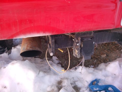1979 Ford Bronco - Close-up of a trailer hitch and exhaust pipe on a red vehicle, with snow on the ground.