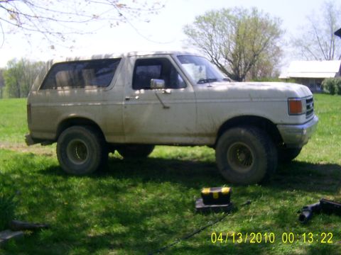 1990 Ford Bronco - This white Ford Bronco, likely from the late 1980s, sits on a grassy field with a toolbox nearby.