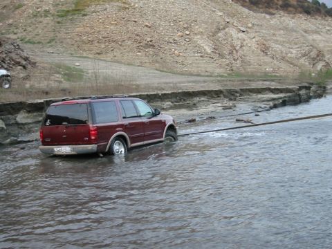 1985 Ford Bronco - A maroon Ford Expedition is stuck in water and being towed out. Another vehicle is visible in the background.