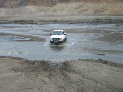 1985 Ford Bronco - A white pickup truck navigates through a water crossing in a barren, mountainous area.