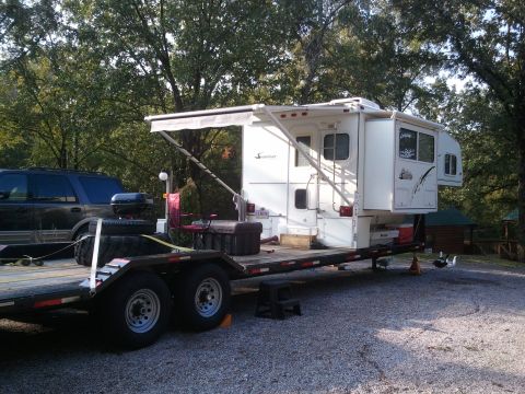 1967 Ford Mustang - A truck camper is loaded onto a flatbed trailer, with a dark SUV visible to the left.