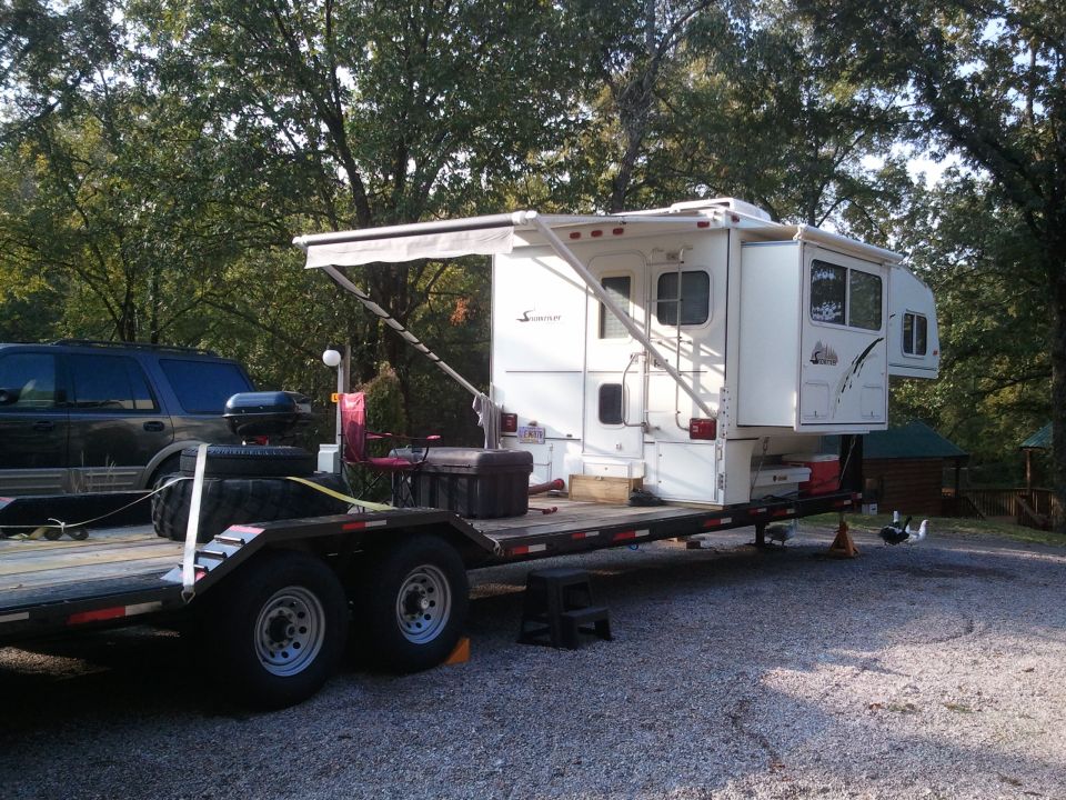 Truck camper on a flatbed trailer with an SUV parked nearby