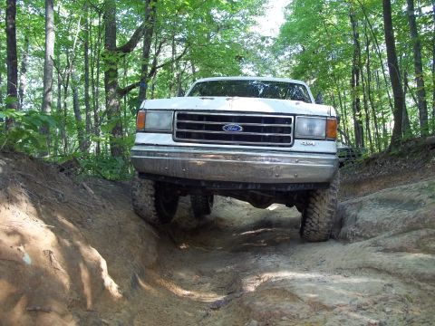 1990 Ford Bronco - A white Ford truck navigates a challenging dirt path through a wooded area.