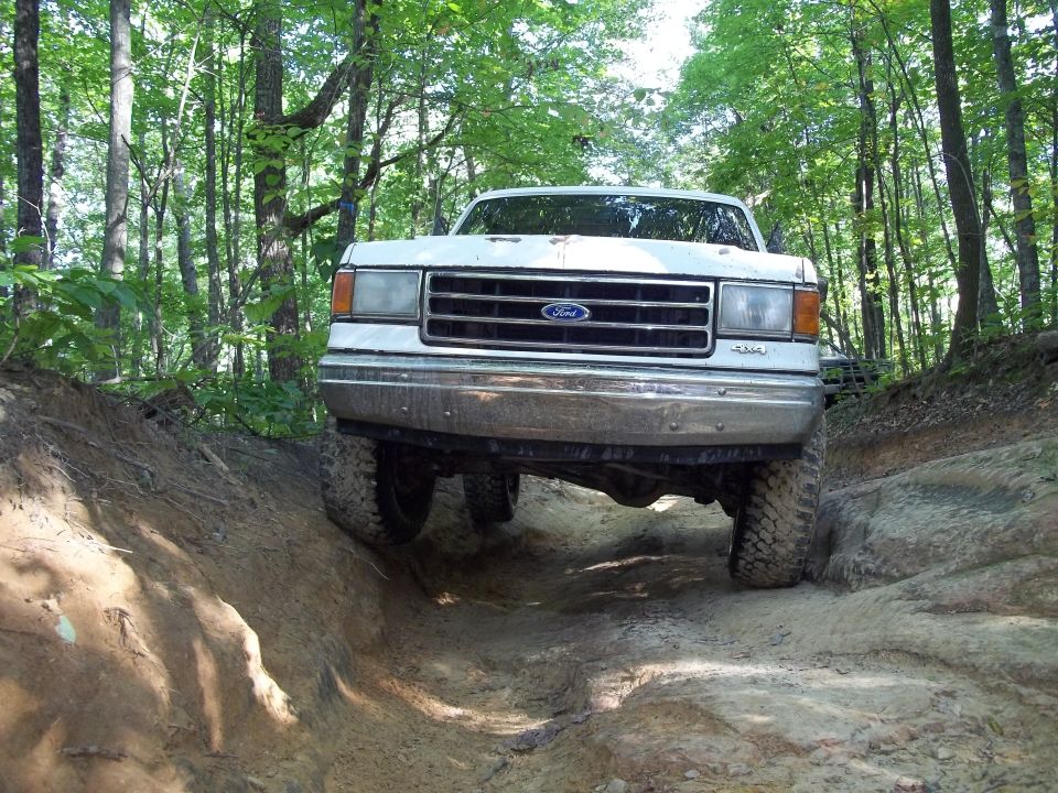 White Ford truck on a dirt trail, front view. Grille and headlights visible