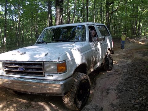 1990 Ford Bronco - White 1990 Ford Bronco navigating a dirt path in a wooded area.