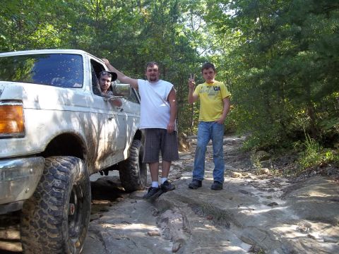 1990 Ford Bronco - Three people pose with a white 1990 Ford Bronco on a rough, wooded trail.