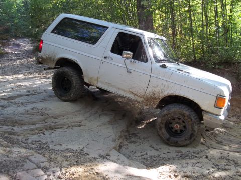 1990 Ford Bronco - A white 1987 Ford Bronco navigates a challenging rocky and muddy off-road path.