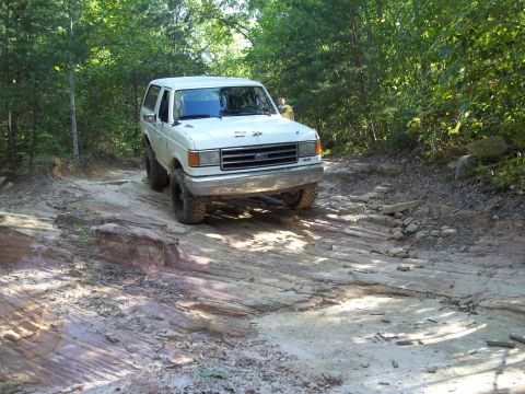 1990 Ford Bronco - This 1990 Ford Bronco navigates a challenging rocky path surrounded by trees.