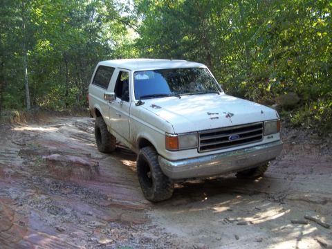 1990 Ford Bronco - White 1990 Ford Bronco navigating a challenging off-road path.