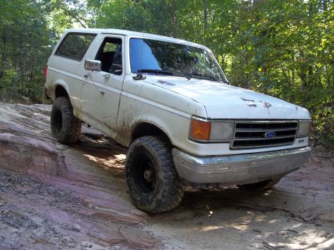 1990 Ford Bronco - This 1990 Ford Bronco is navigating a challenging off-road path with mud splattered on its body.