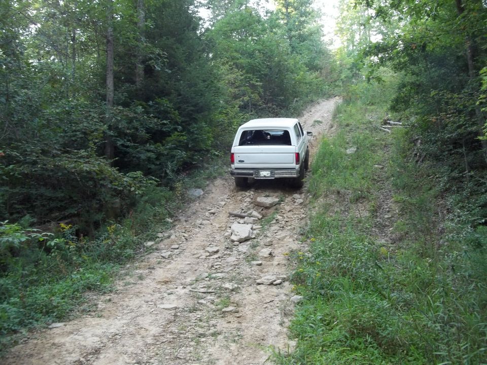 1990 Ford Bronco driving up a rocky, wooded trail