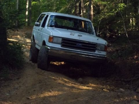 1990 Ford Bronco - White 1990 Ford Bronco navigates a wooded dirt trail.