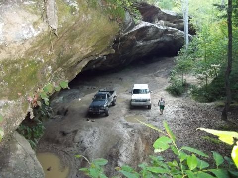1990 Ford Bronco - Two vehicles navigate a challenging, muddy trail near a large rock formation.