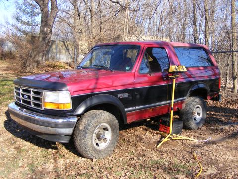 1995 Ford Bronco - This Ford Bronco is parked outdoors on a dirt and leaf-covered surface.