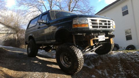 1995 Ford Bronco - This lifted 1995 Ford Bronco features a dark exterior and aggressive off-road tires, captured in a three-quarter front perspective.