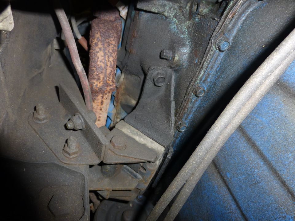 Engine mount bracket bolted to engine block, with rusty exhaust pipe nearby