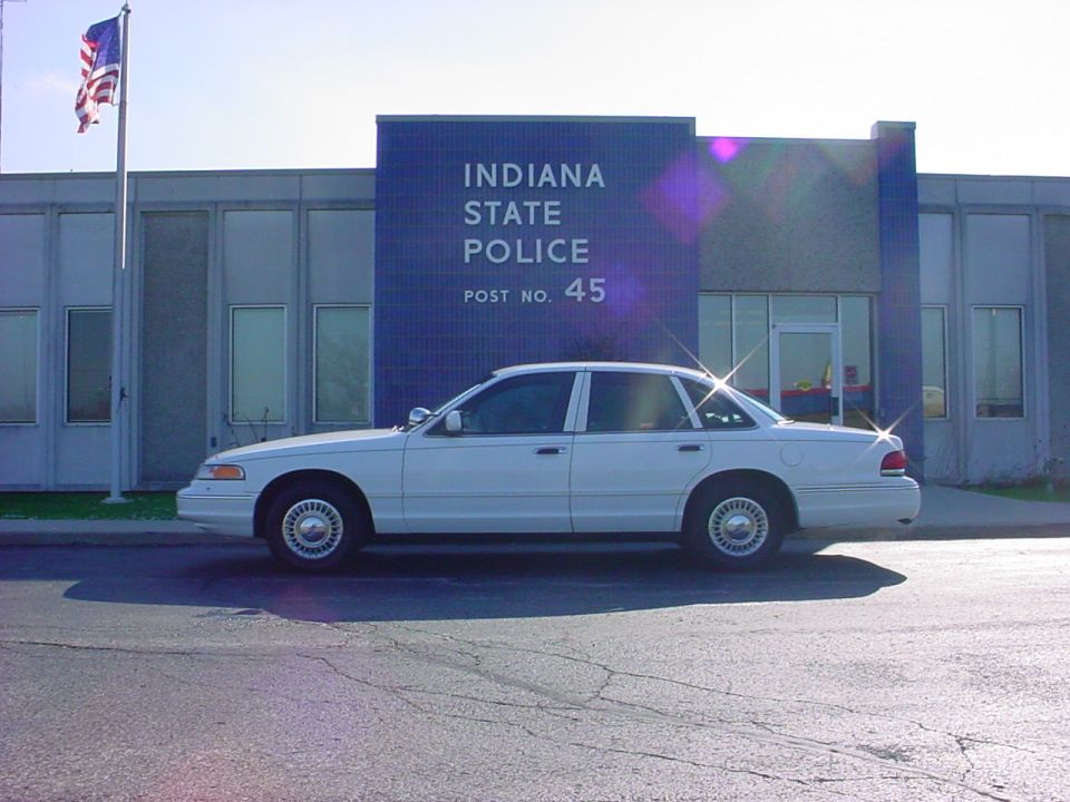 White police sedan parked in front of Indiana State Police Post No. 45. The car appears to be a 1998 model