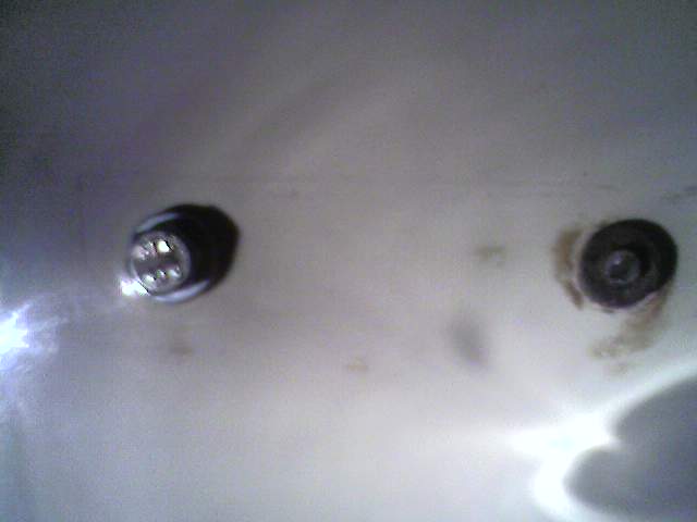 Two black grommeted fasteners on a white panel, one with rust stains around it